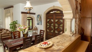 A dining area with a long wooden table, chairs, a vase with flowers, and a clock on the wall. - villa Gregory (Chania)