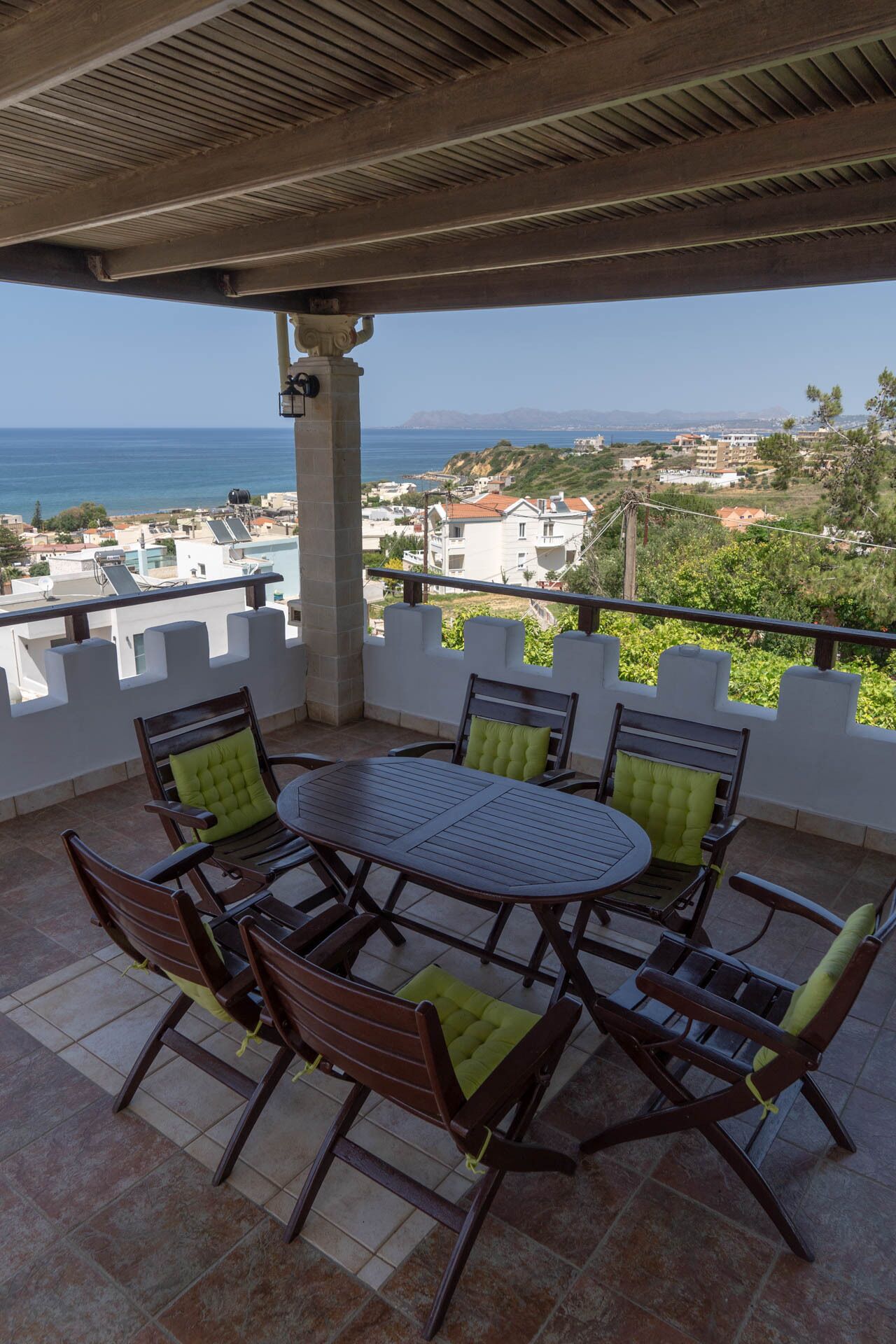 Een overdekt terras met tafel en stoelen, met uitzicht op de kust.