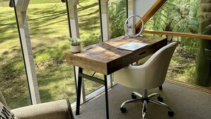 Ein moderner Arbeitsraum mit Schreibtisch, Stuhl und großen Fenstern mit Blick auf eine Rasenfläche.