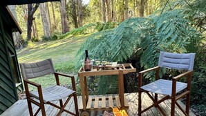 Eine Holzterrasse mit zwei Stühlen, einem kleinen Tisch, einer Feuerstelle und einer Weinflasche.