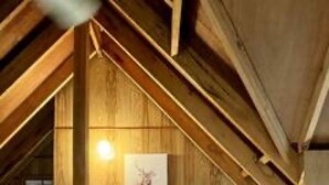 Ein gemütliches Schlafzimmer im Dachgeschoss mit Holzbalken, einem Bett, einem Fernseher und Aufbewahrungsboxen.