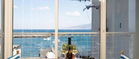 A table with a bottle of wine, glasses, and seafood in a room with a view of the sea.