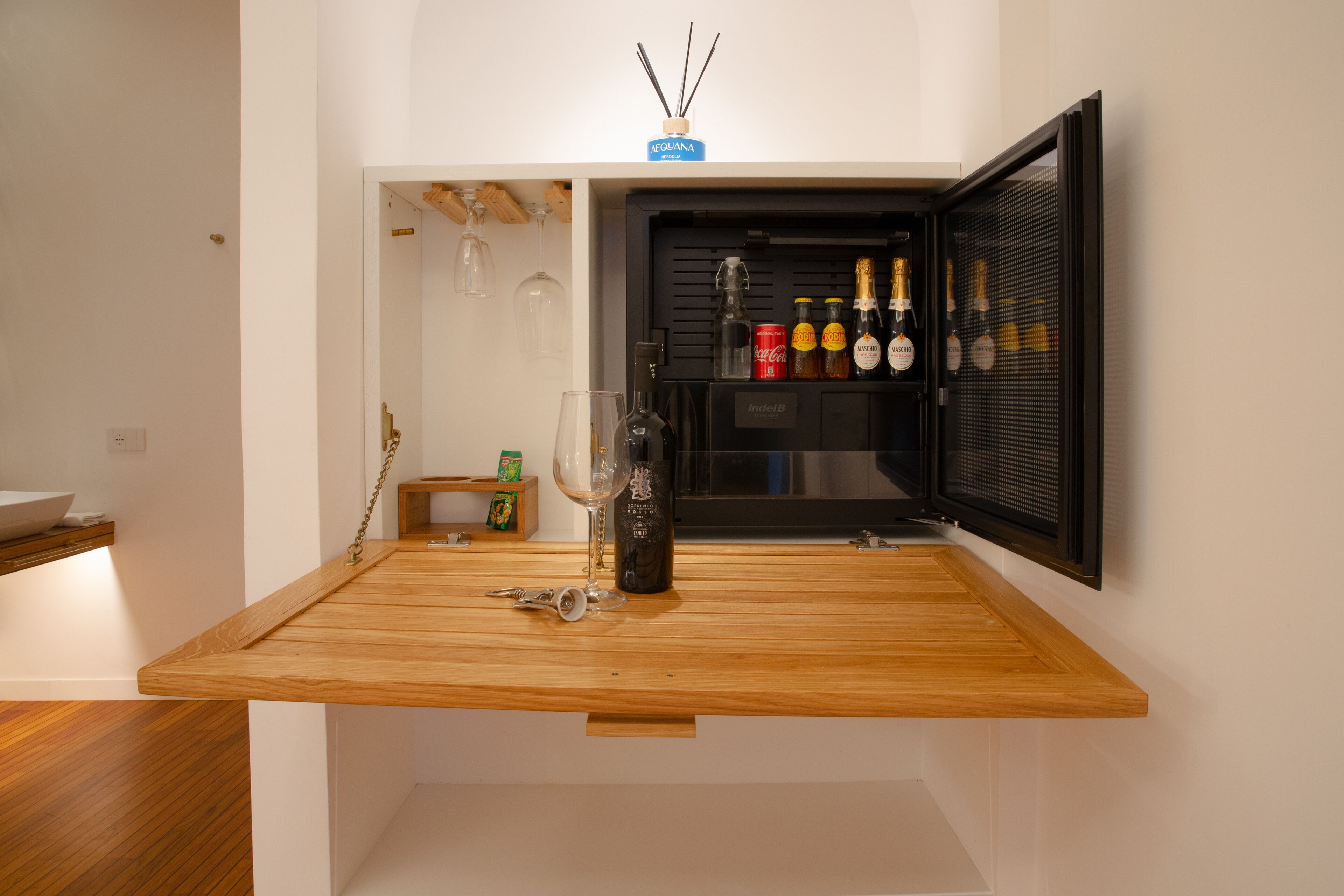 A compact kitchen with a wooden countertop, a wine bottle, and a minibar with various bottles and glasses.