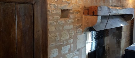 A rustic stone wall with a wooden door and a fireplace with logs.