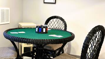 Une table ronde recouverte d’un drap de feutre vert, entourée de quatre chaises dont les dossiers sont en osier noir et les assises présentent un motif décoratif.