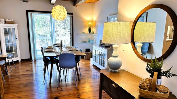 Un coin repas avec une table en bois dressée pour quatre personnes, entourée de chaises. Un grand miroir est accroché au mur et reflète la pièce.