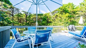 Une terrasse en bois avec une table ronde et des chaises, un parasol et un barbecue.
