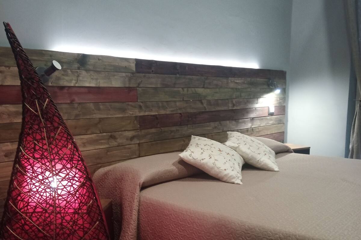 A bedroom with a wooden headboard, a bed with a beige blanket, and a red decorative object.