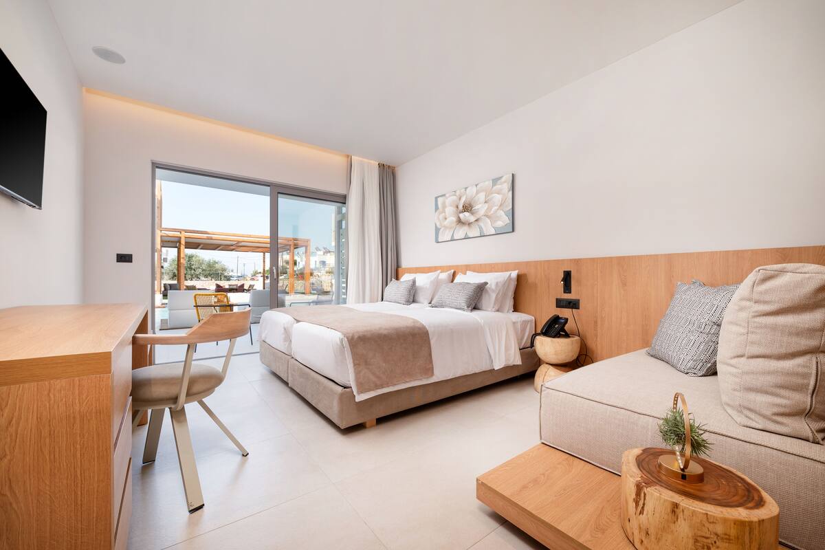 A modern hotel room with a bed, a sofa, a desk, and a dining area.