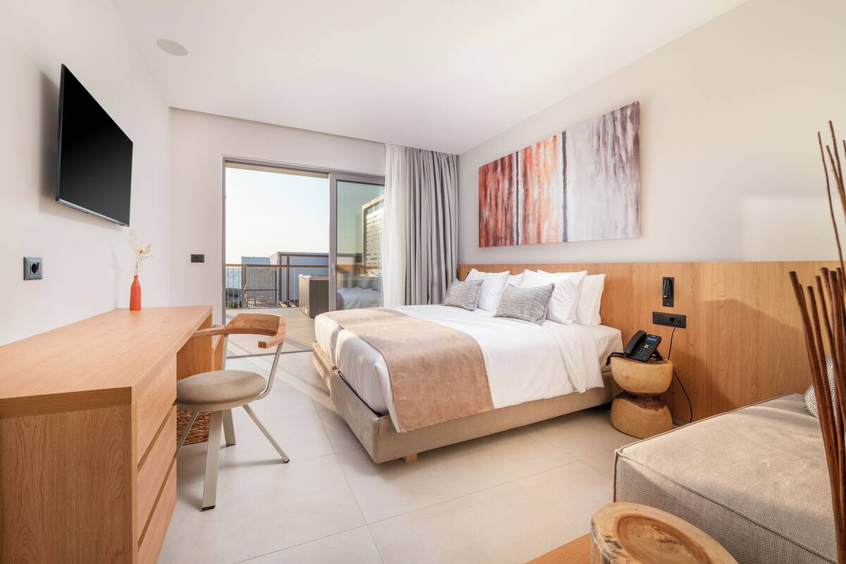 A modern hotel room with a bed, desk, and chair, a flat-screen TV, and a large window with a view.
