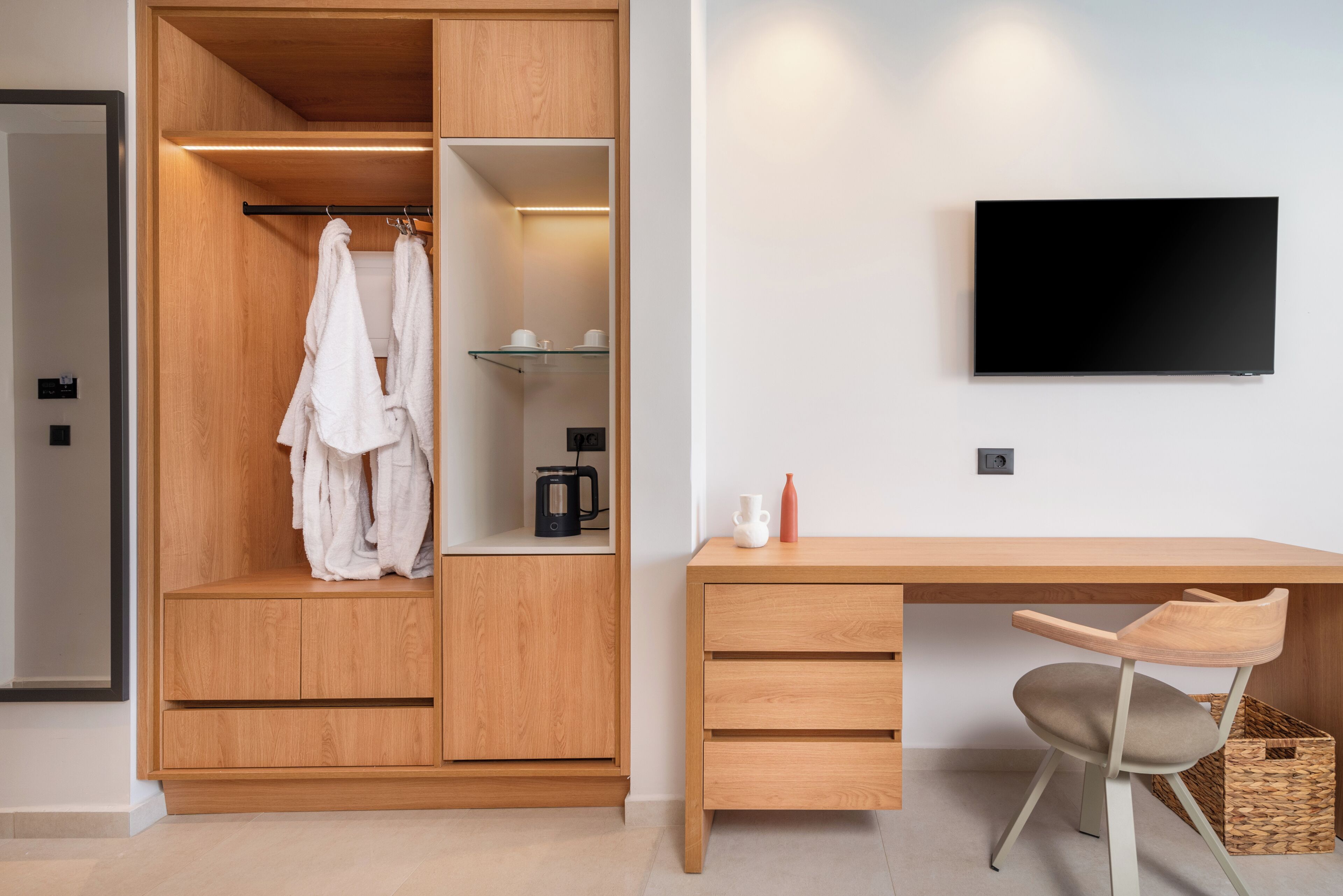 A modern room with a wooden wardrobe, a desk with a chair, and a mounted TV.