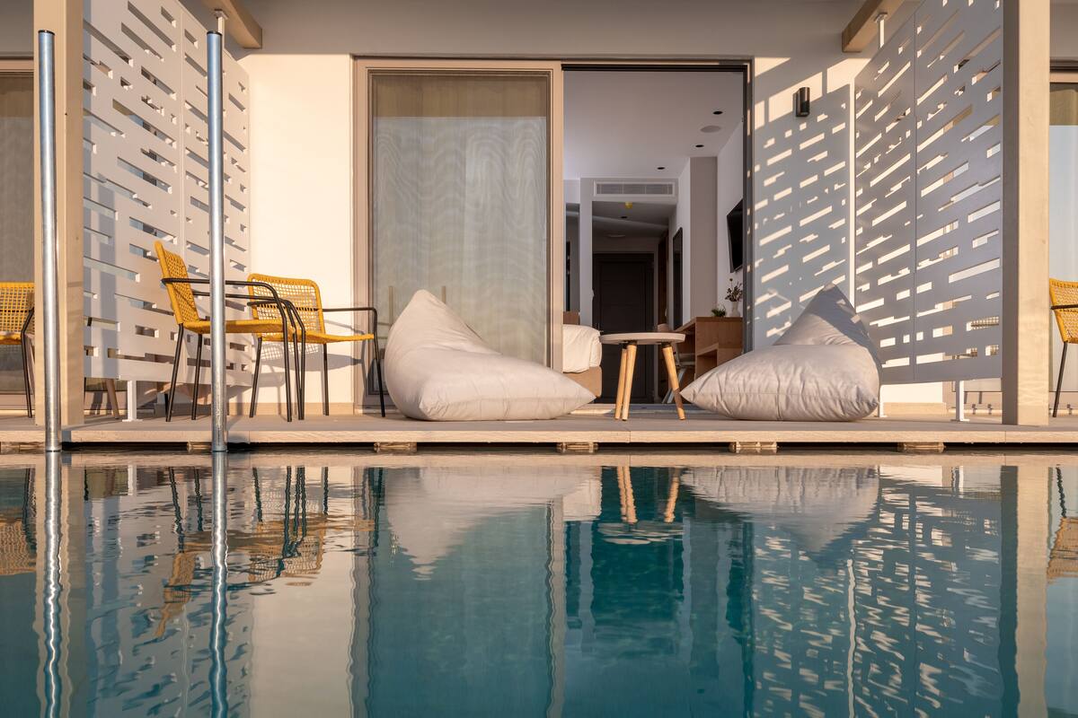 A modern outdoor pool area with a clear view of the pool, two yellow chairs, and a table with a cushion.