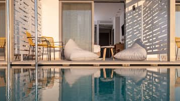 Un área de piscina moderna al aire libre, con vista despejada, dos sillas amarillas y una mesa con cojín.