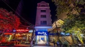 Et hotel med en markant indgang, et skilt med 'Hong Kong Hotel' og tilstødende butikker, heriblandt en pizzeria og en café.