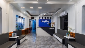 Et hotelreceptionsområde med et blåt skilt der viser "Hong Kong Hotel", en receptionsdisk, siddepladser og en marmorgulv.