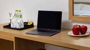 En bærbar computer på et træbord med en bakke, der indeholder en flaske, et tesæt og en kaffepakke. To æbler ligger på en tallerken ved siden af computeren.