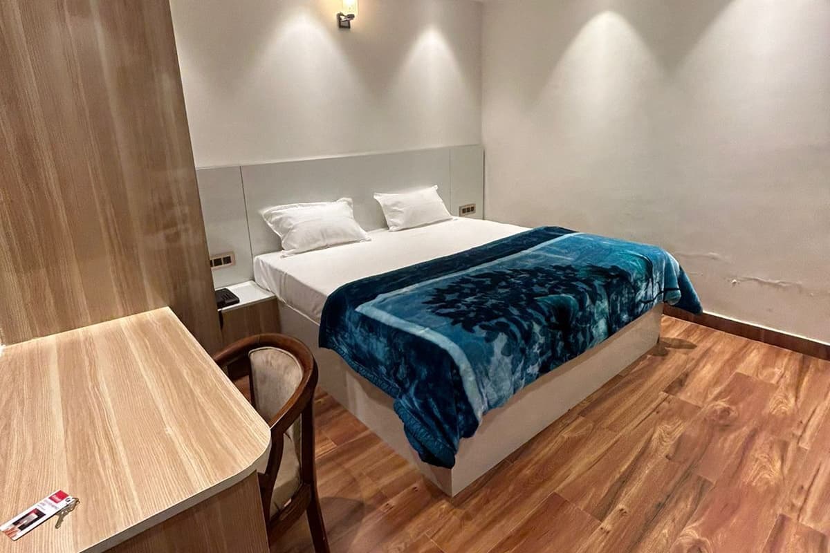 Hotellihuone, jossa on sänky, puulattia, kattotuuletin ja yöpöytä.