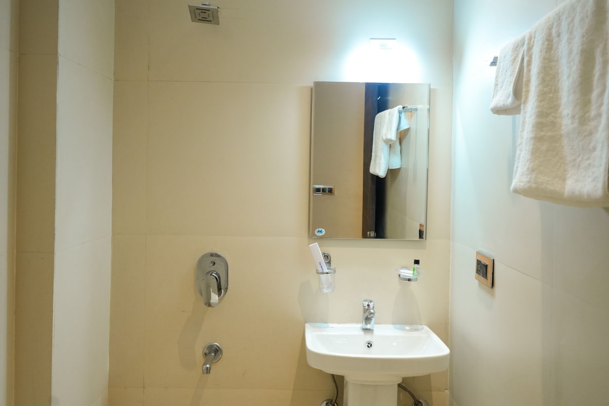 A bathroom with a sink, mirror, towel rack, and a shower control panel.