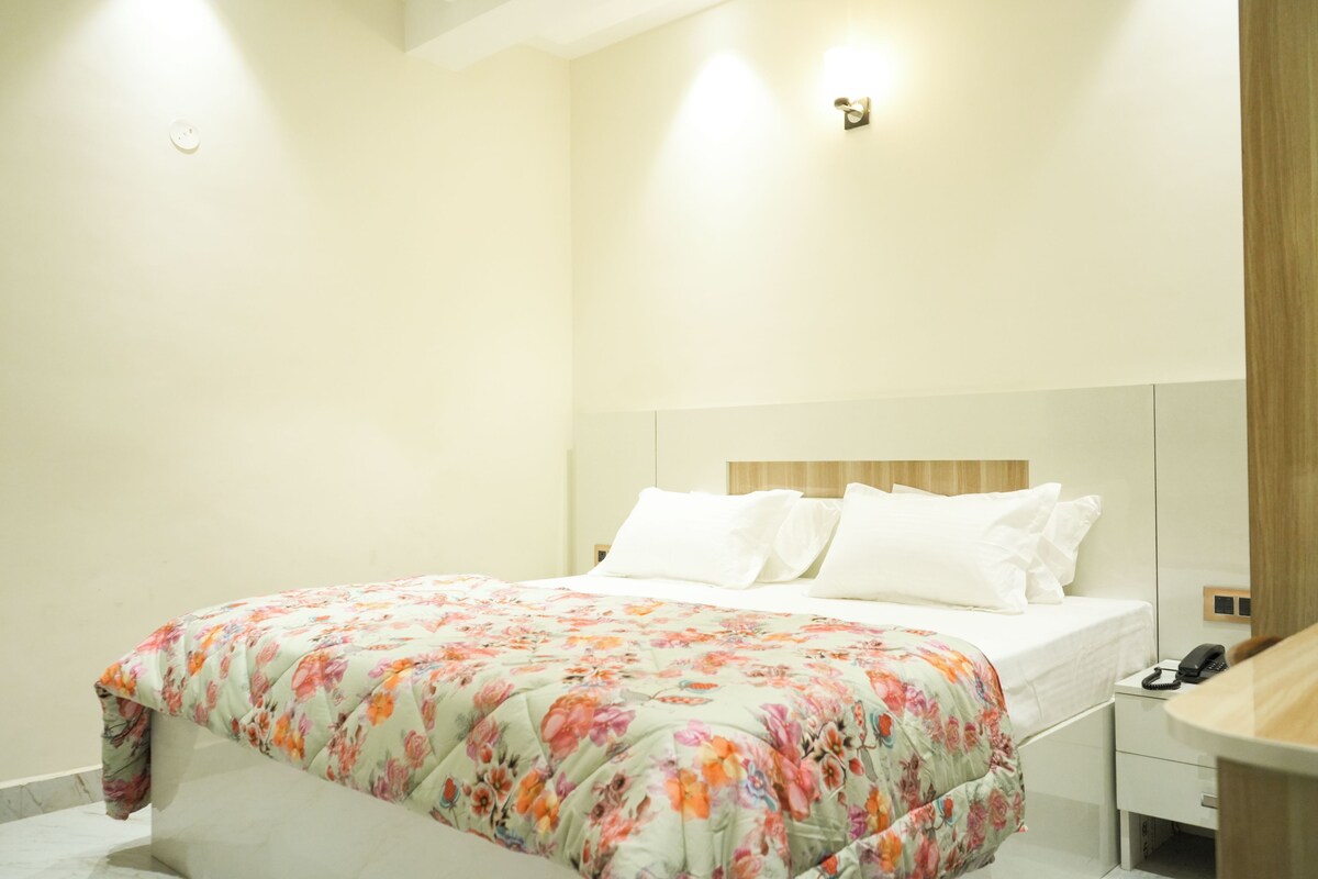 Een net opgemaakt bed met een bloemenprint deken, een nachtkastje met een telefoon, en een houten hoofdbord.