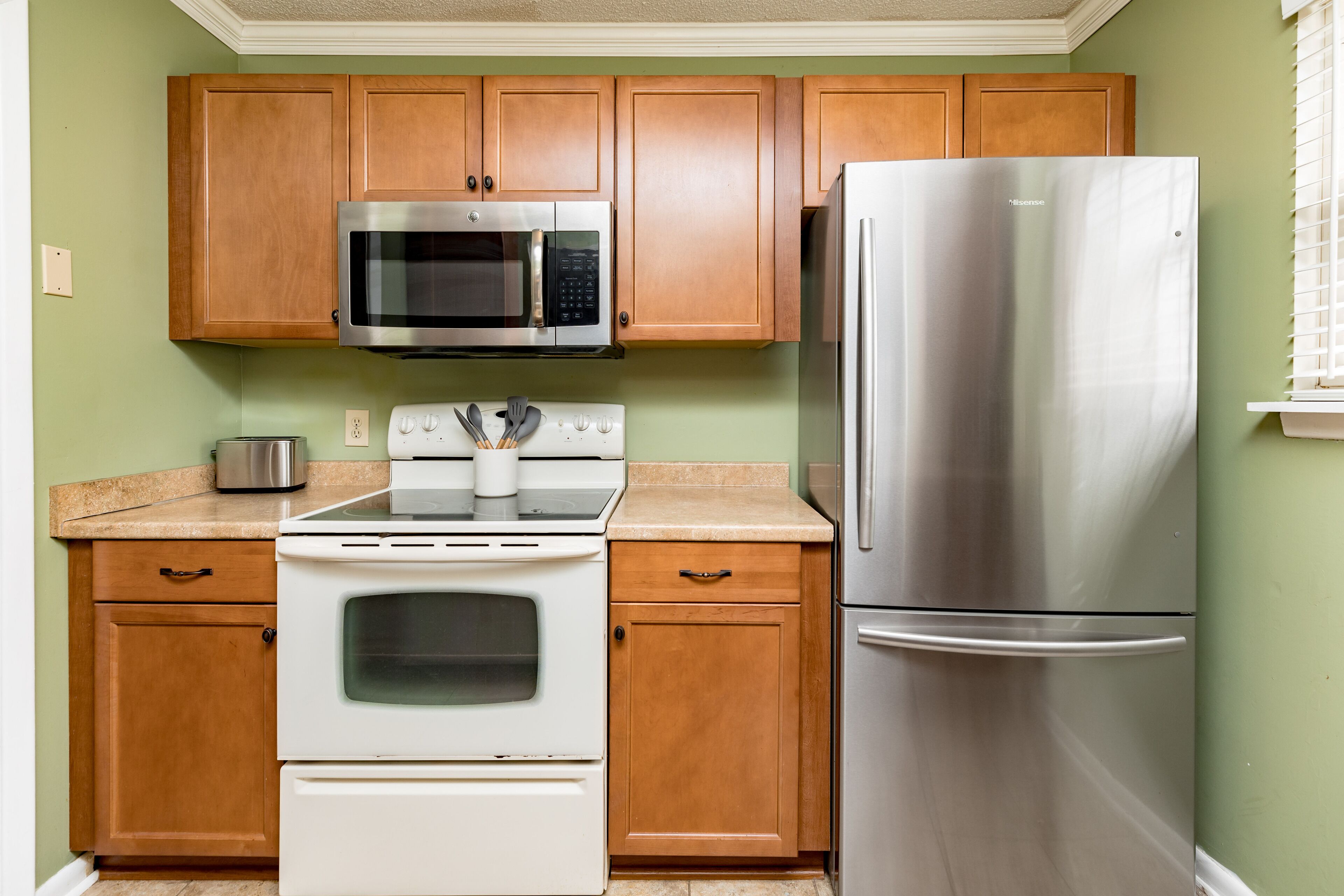 Una cocina con armarios de madera, un refrigerador de acero inoxidable, un microondas, un horno y un tostador.