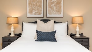 A neatly made bed with white and blue pillows, two bedside lamps, and two framed botanical prints on the wall. - Central 2BR/2BA | Pet Friendly | Fenced Yard (Warner Robins)