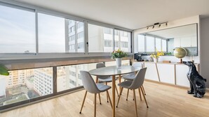 A modern apartment with a balcony, a dining area with a round table and chairs, a kitchen with a globe and flowers, and a black dog sitting on the floor.