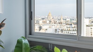 A room with a large window overlooking a cityscape, a potted plant, and a white chair.