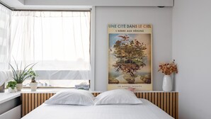 A neatly made bed with white bedding, a window with sheer curtains, and a poster of a tree on the wall.