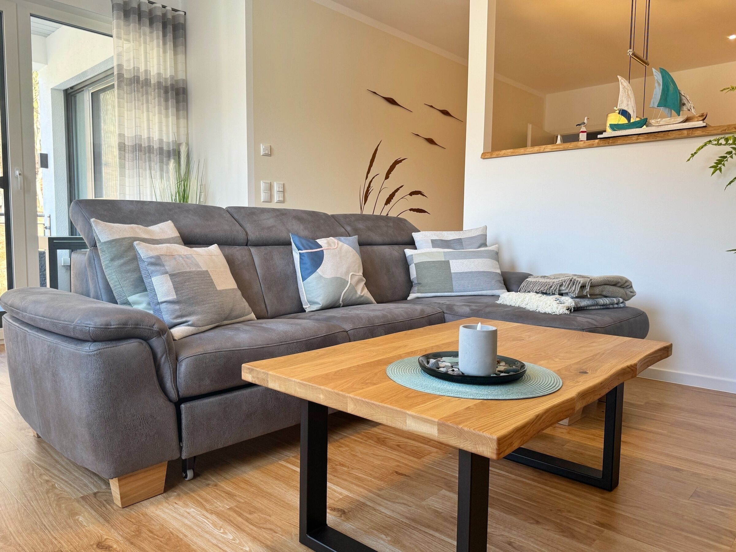 Ein modernes Wohnzimmer mit grauem Sofa, einem Holztisch und einem dekorativen Segelboitschrank.