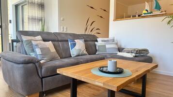 Ein modernes Wohnzimmer mit grauem Sofa, einem Holztisch und einem dekorativen Segelboitschrank.