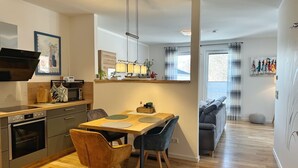 Eine moderne Küche mit Essbereich, Holzboden und Blick auf ein Wohnzimmer mit Sofa und Kunstwerken.
