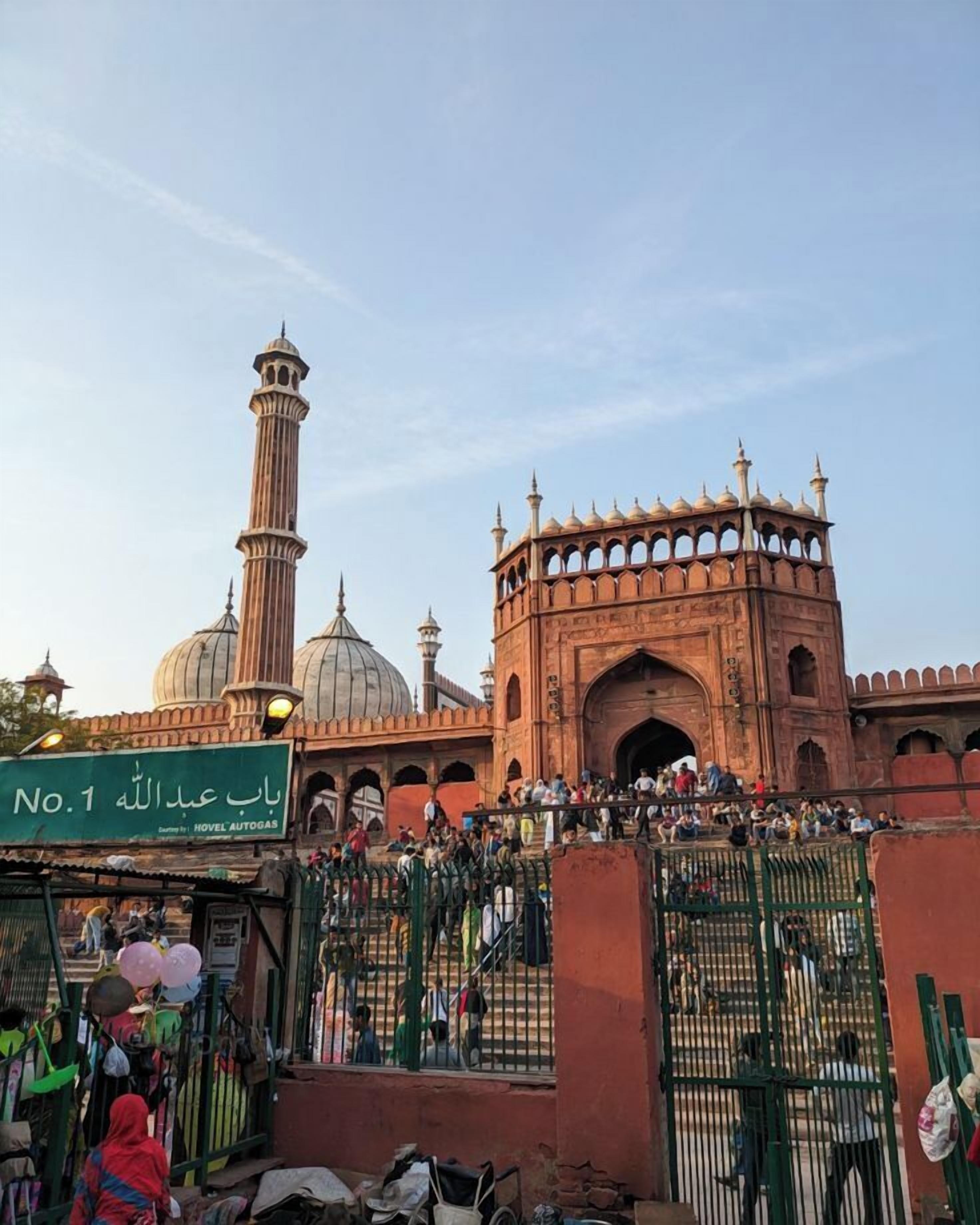 A historic building with domes and minarets, a large gate, and a crowd of people.