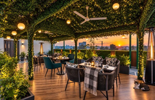 An outdoor seating area with tables, chairs, and a ceiling fan. - HOTEL UPTOWN - Luxury Restaurant & Rooftop Near Connaught Place (New Delhi)