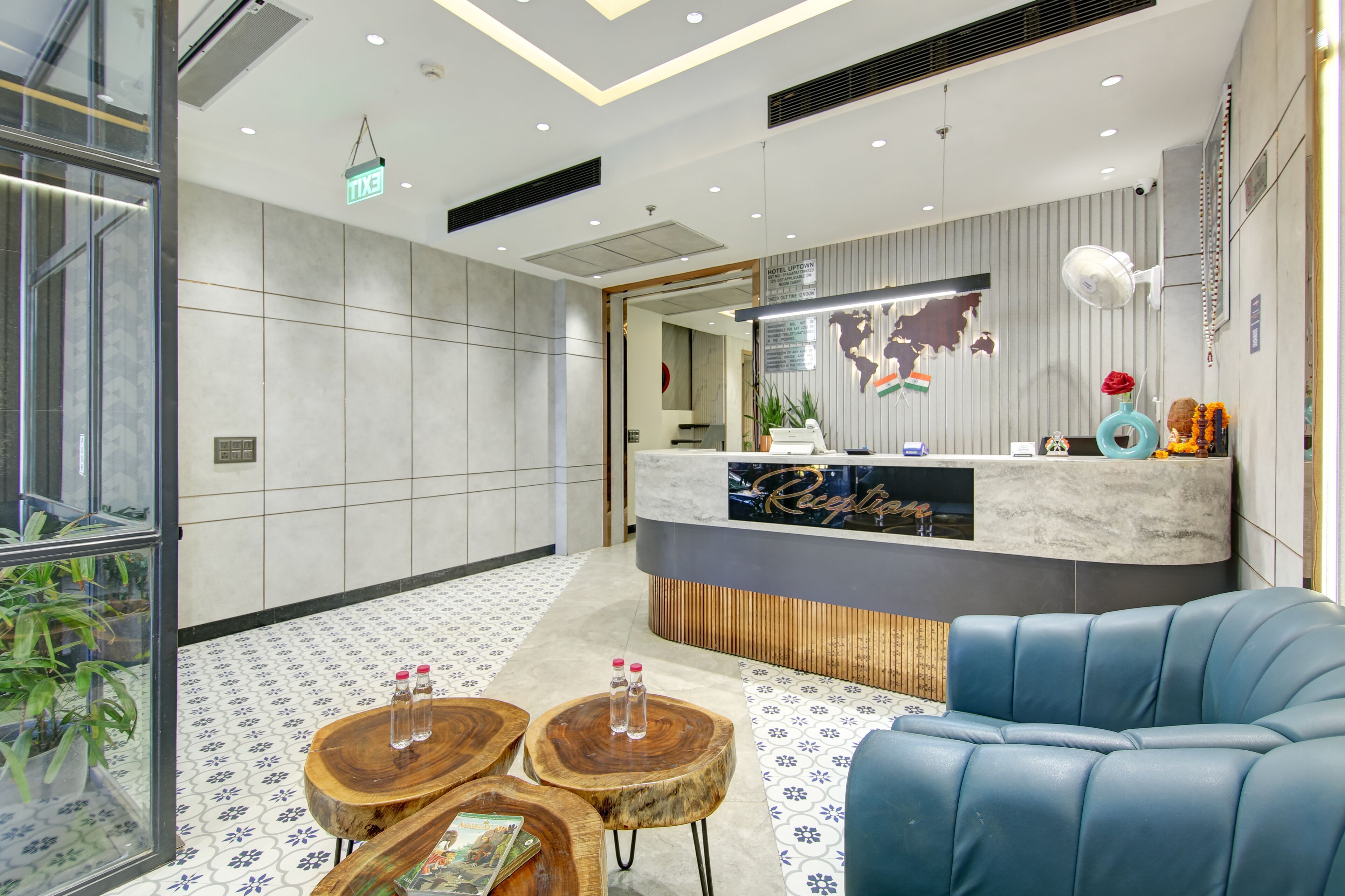Un espace d’accueil moderne avec un comptoir en marbre, un canapé en cuir bleu, des tables en bois avec des bouteilles d’eau et une carte du monde décorative accrochée au mur.