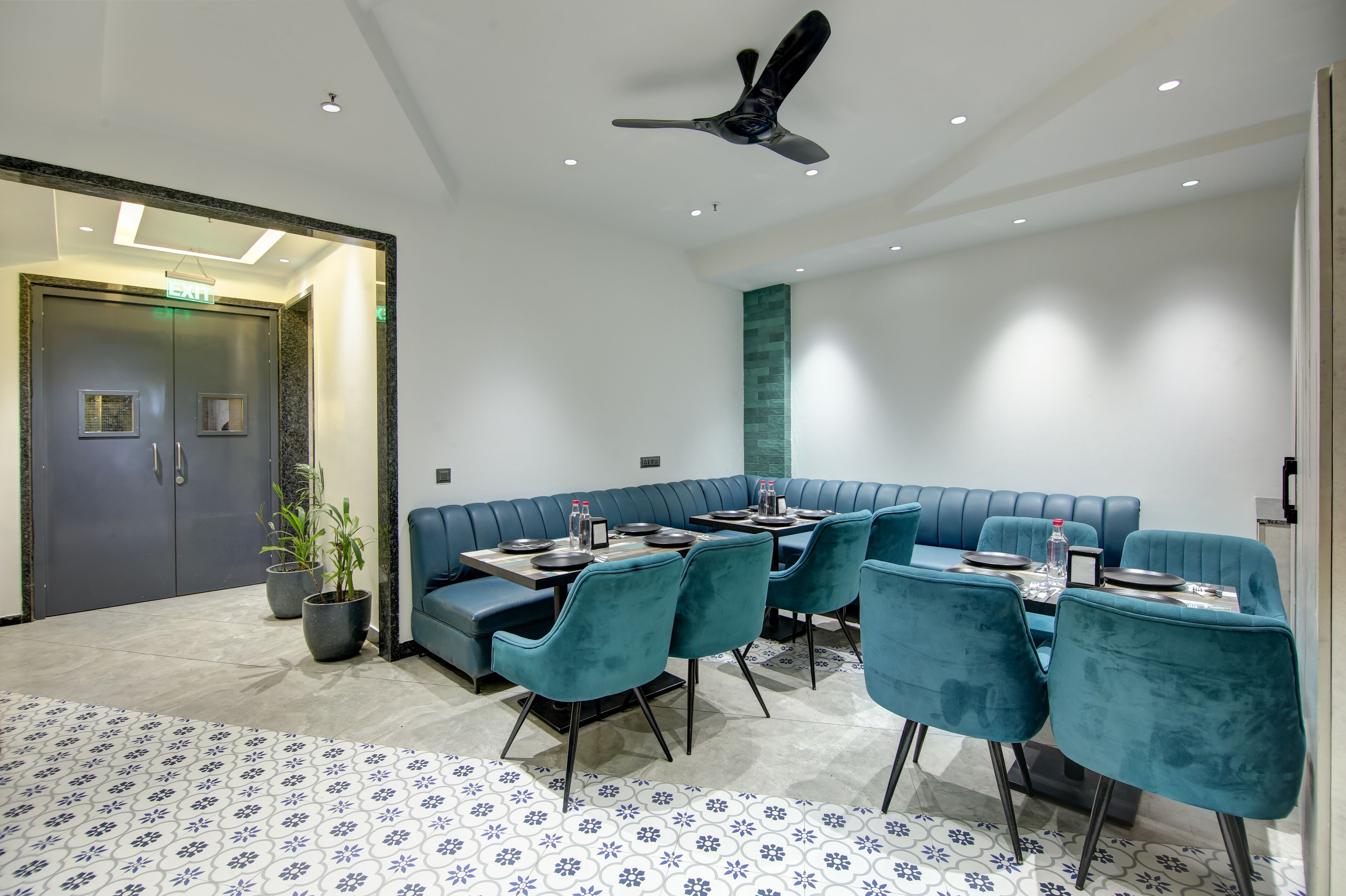Ein modernes Restaurant mit einer blauen Sitzbank, einem Esstisch mit Stühlen und einem Deckenventilator.