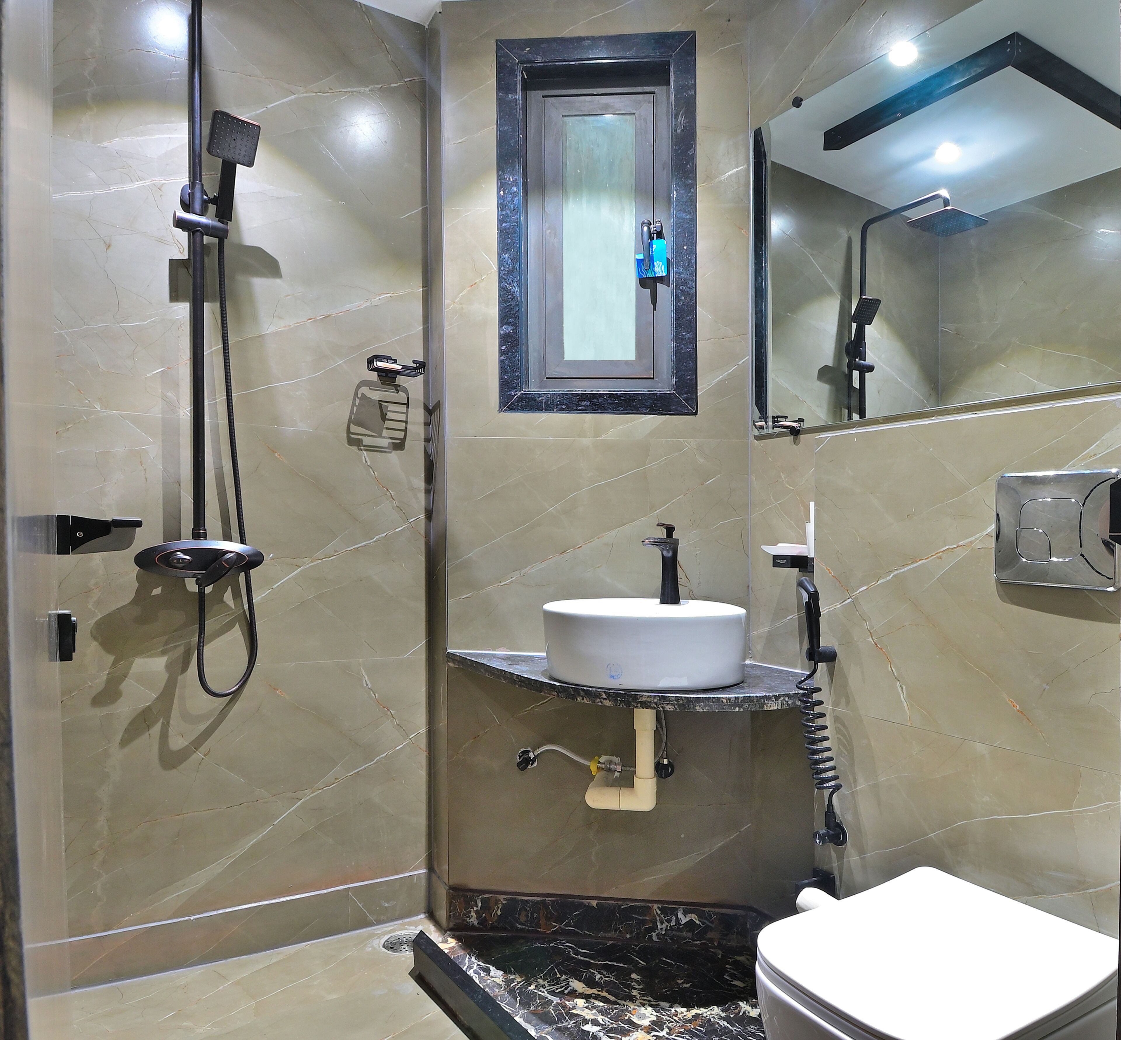 Un bany amb sòl de marbre, un lavabo blanc, un mirall, una dutxa i un vàter.