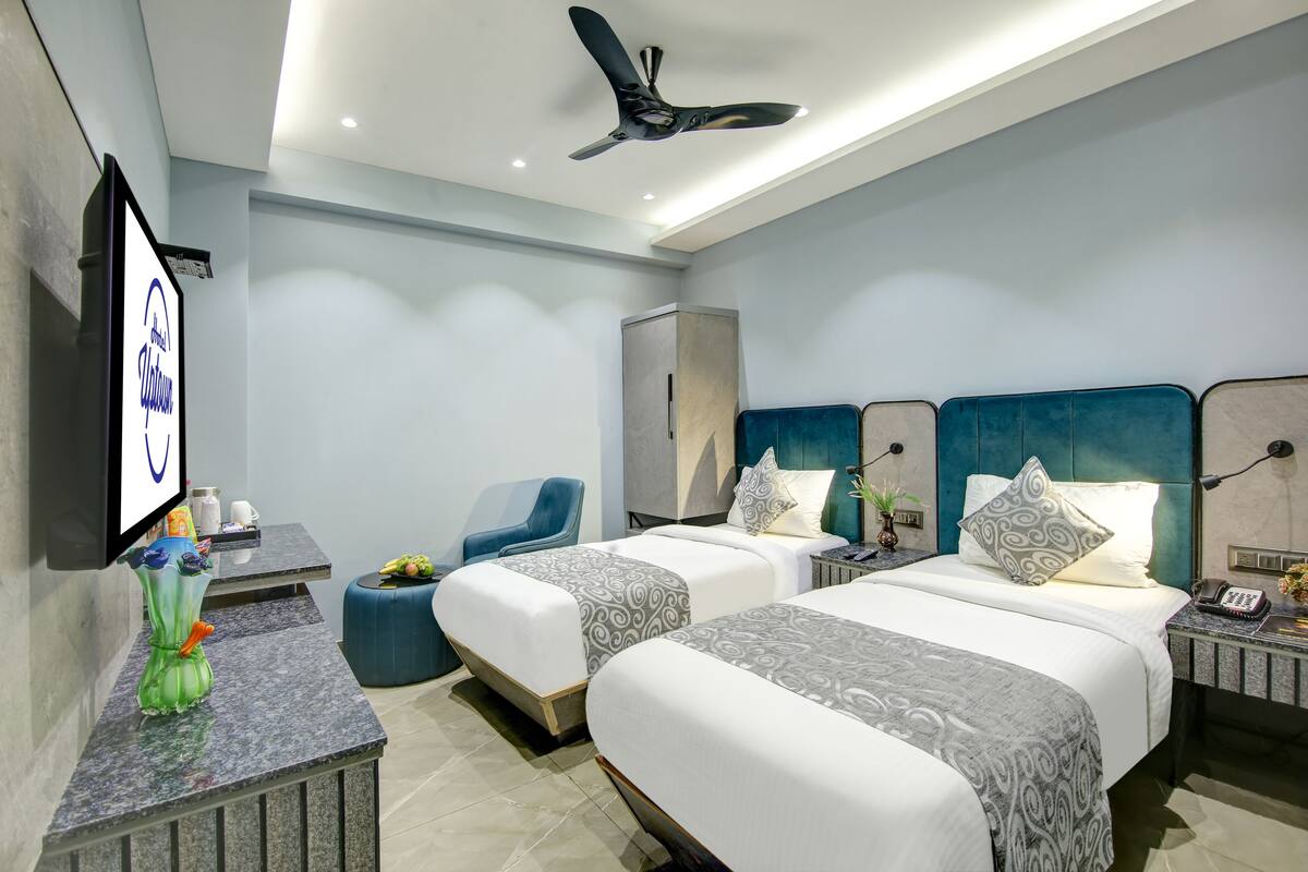 A modern hotel room with two beds, a desk, a chair, and a TV.