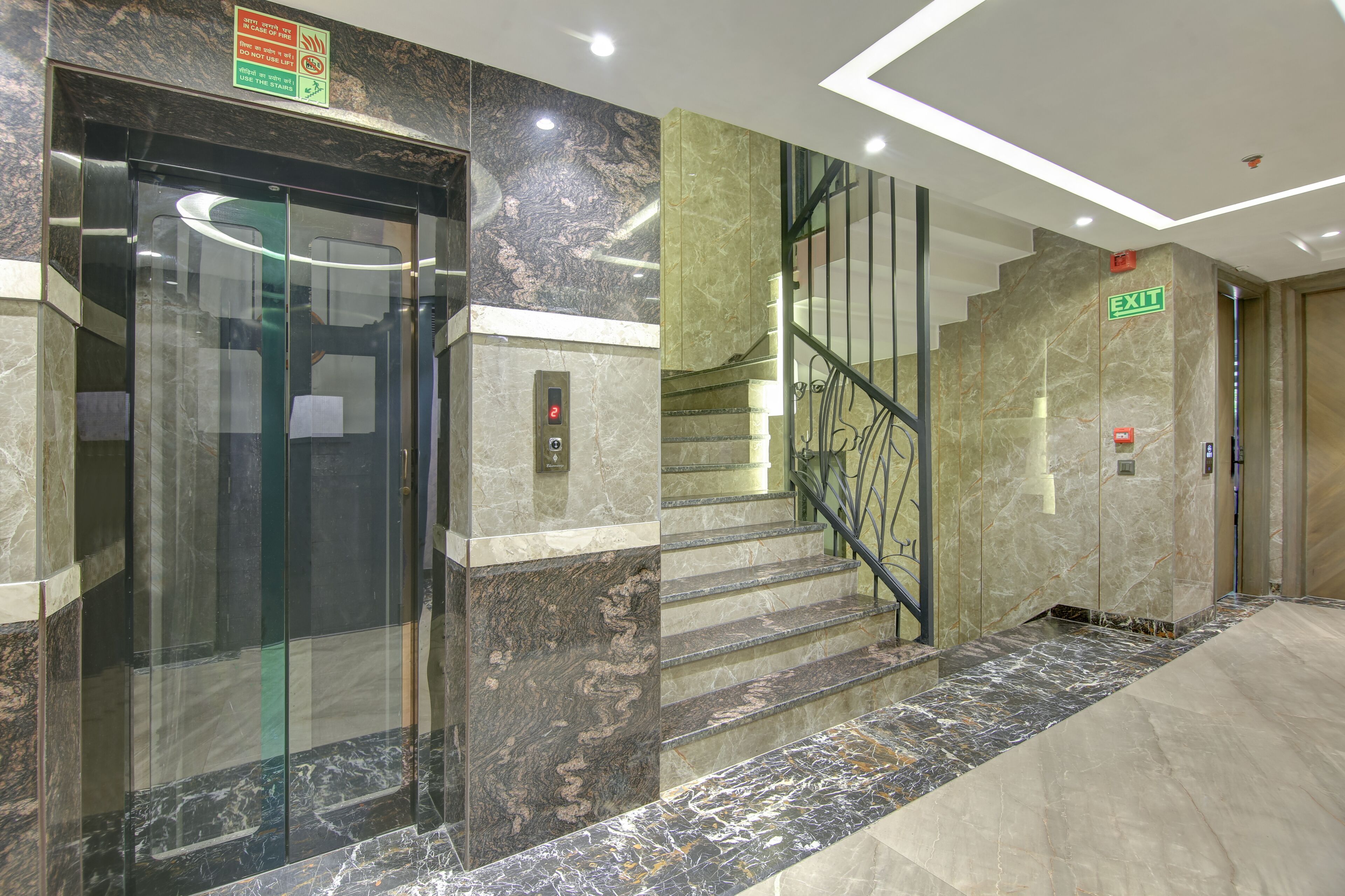 Ein Aufzug mit Glastür, Marmorwänden und einer Treppe mit Metallgeländern.