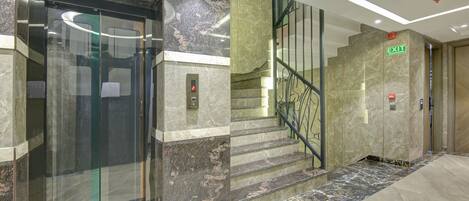 Ein Aufzug mit Glastür, Marmorwänden und einer Treppe mit Metallgeländern.