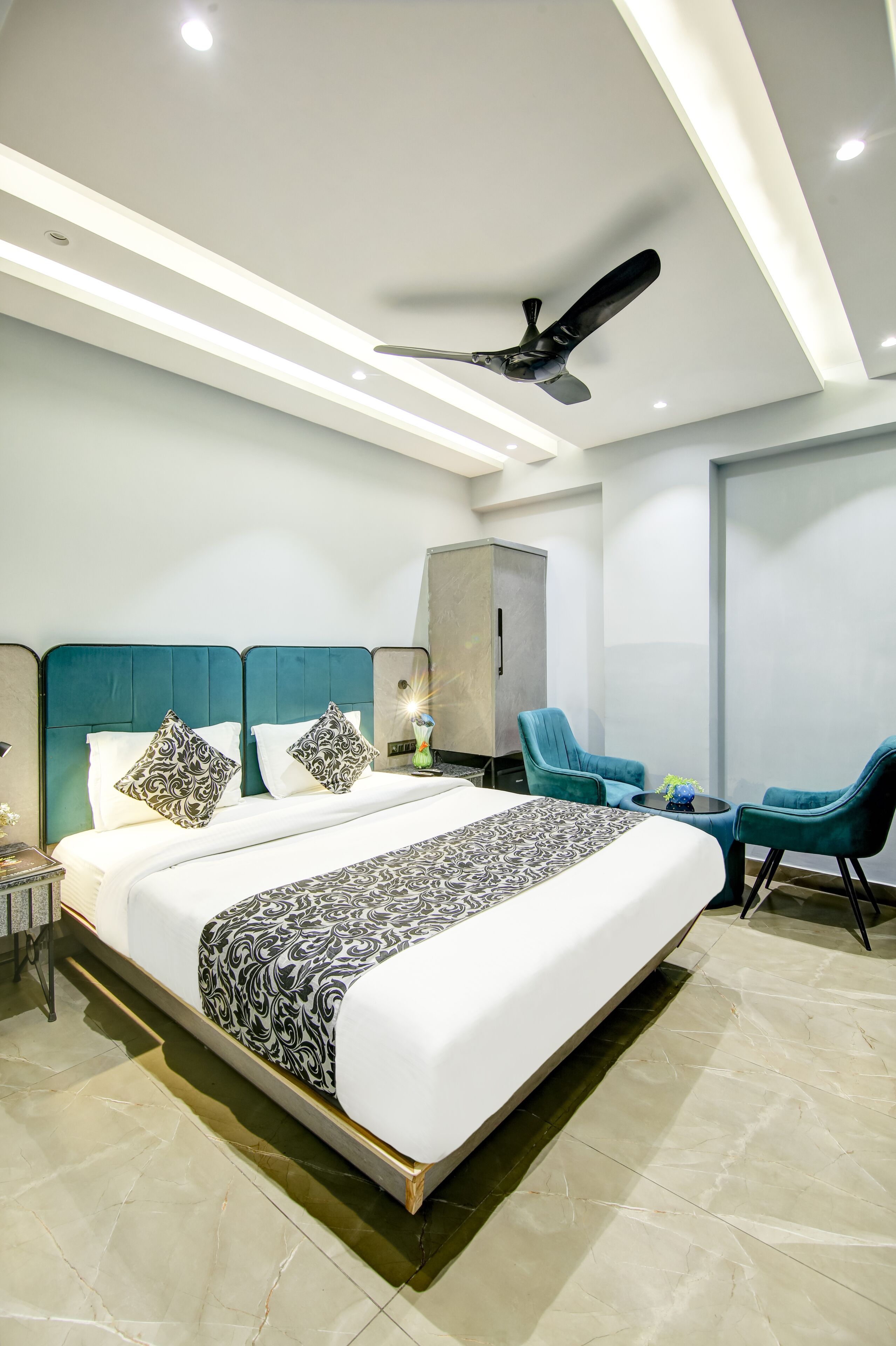 A modern hotel room with a large bed, a ceiling fan, and two chairs.