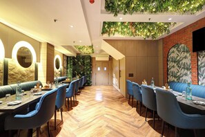 A restaurant with wooden flooring, blue upholstered booths, and a brick wall with a mural. - HOTEL UPTOWN - Luxury Restaurant & Rooftop Near Connaught Place (New Delhi)