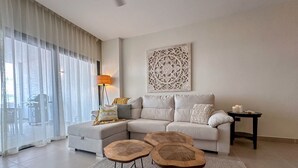 A modern living room with a sectional sofa, two wooden stools, a floor lamp, and a decorative wall piece. - Incredibly Beautiful condo just steps to the beach (Punta Cana)