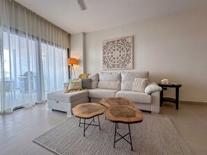 A modern living room with a sectional sofa, two wooden stools, a floor lamp, and a decorative wall piece.