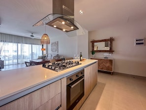 A modern kitchen with a central island, built-in oven, and a dining area with a sofa and table. - Incredibly Beautiful condo just steps to the beach (Punta Cana)