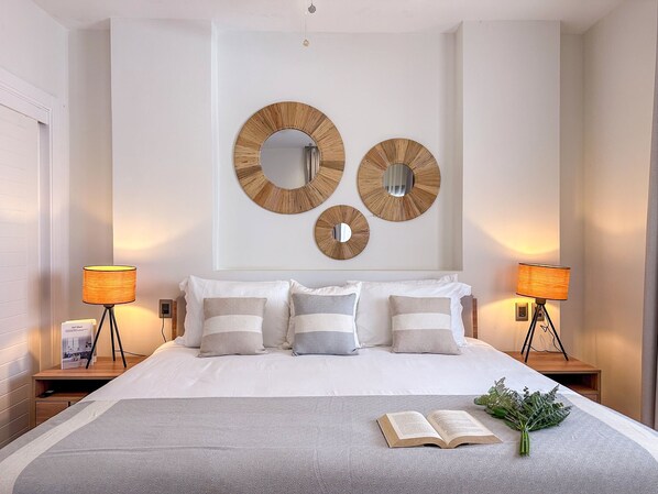 A neatly arranged bedroom with a large bed, two bedside tables, and three wall-mounted mirrors.