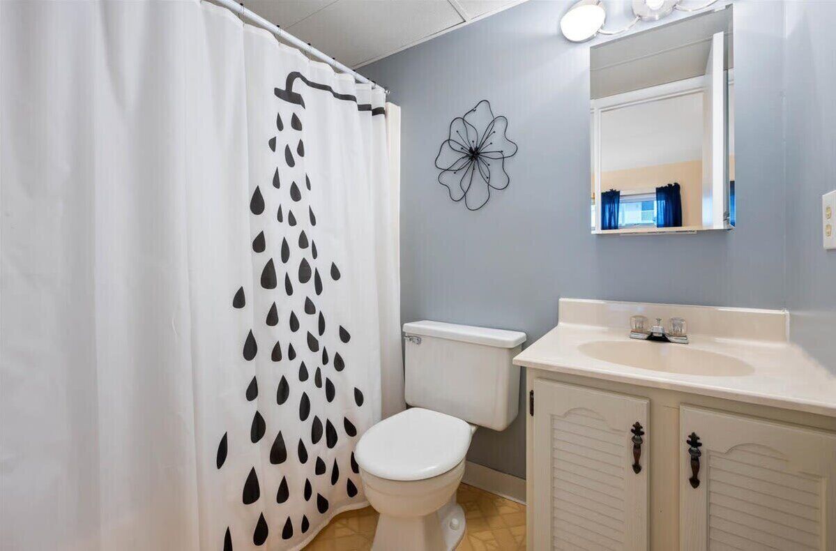 A bathroom with a toilet, a sink, a mirror, and a shower curtain with a leaf pattern.
