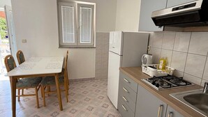 Cocina compacta con una mesa, sillas, refrigerador, estufa y una ventana con persianas.