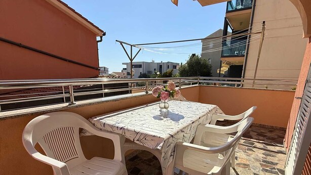 Un balcón con una mesa y sillas, un florero con flores y vistas a edificios al fondo.