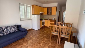 Cocina compacta con muebles de madera, un refrigerador blanco, una mesa de comedor con sillas y un sofá con cojines estampados.