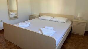 Una cama bien tendida con sábanas y toallas blancas, una mesita de noche con lámpara, una mesita auxiliar y un espejo en la pared.